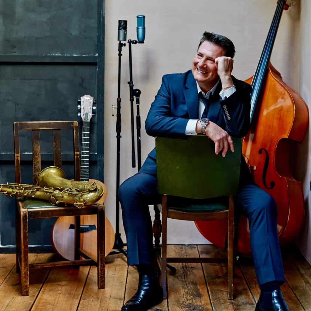 Tony Hadley sits backwards on a chair. Instruments are scattered around him.