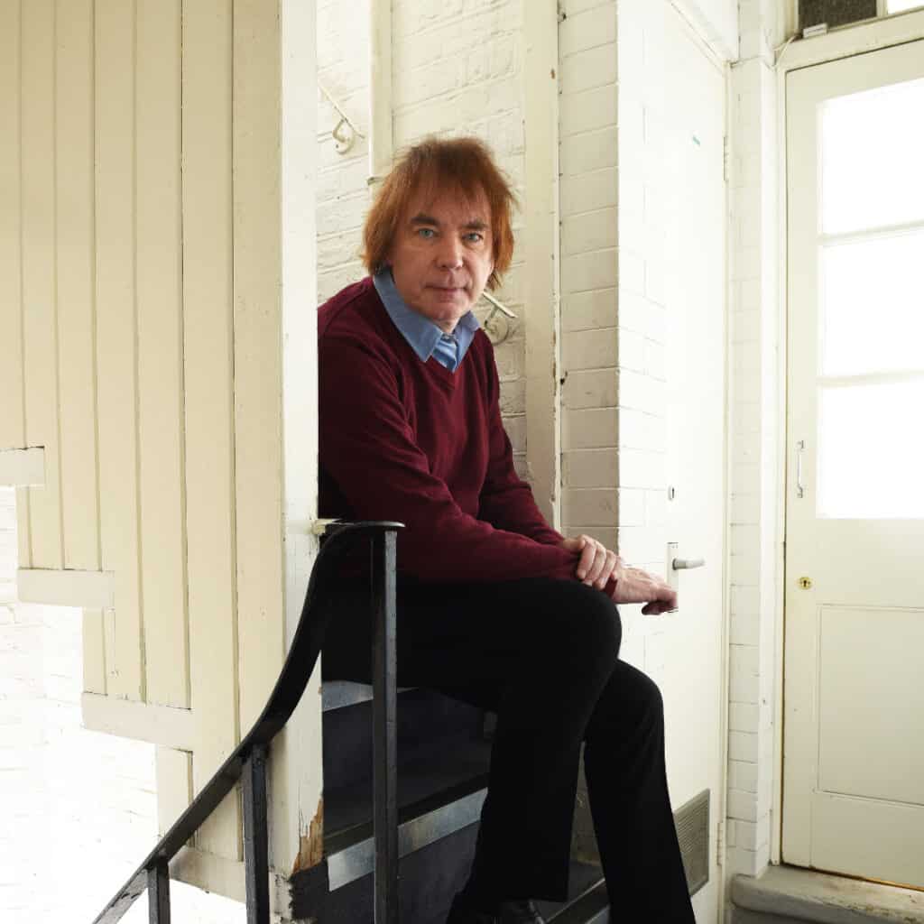Julian Lloyd Webber sits on a set of stairs, looking at the camera.