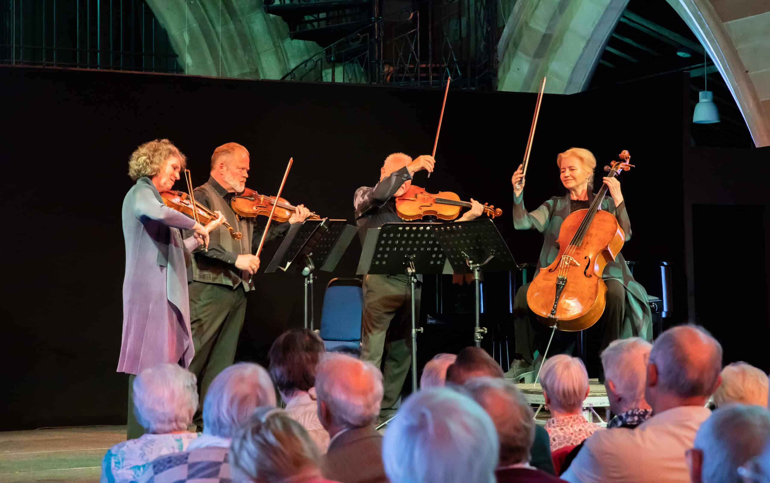 The Brodsky String Quartet stand on stage with bows in the air