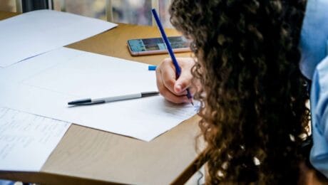 A person with curly hair writes on paper during a book or writing workshop at Lichfield Festival.