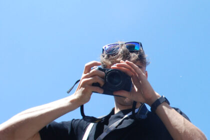 A man hides his face behind a camera, in front of Lichfield Cathedral