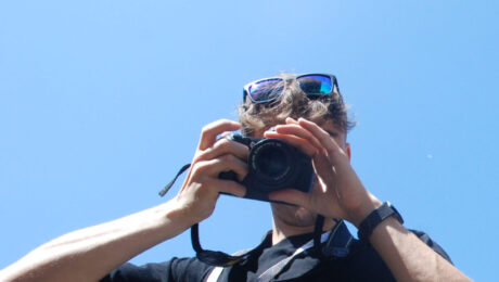 A man hides his face behind a camera, in front of Lichfield Cathedral