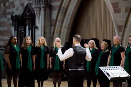 A group of singers in a horseshoe, led by a conductor