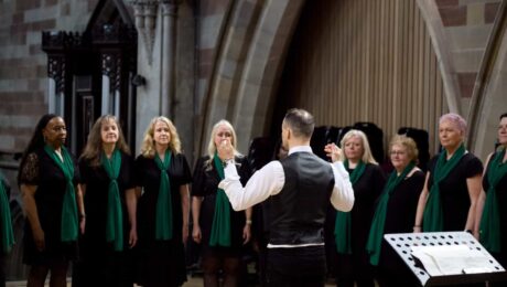 A group of singers in a horseshoe, led by a conductor