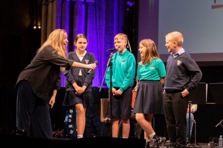 Learning & Participation Primary School students stand on stage and speak into a microphone