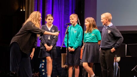 Primary School students stand on stage and speak into a microphone