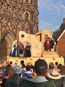 Male actors stand on a small stage wearing Elizabethan costume 