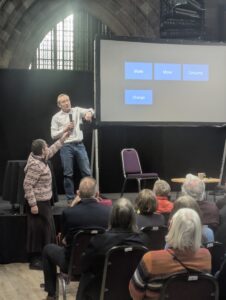 Tim Minshall stands on a stage in front of a audience with a short woman with dark hair standing next to him holding a Nokia phone