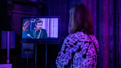 A Festival staff member watches a saxophonist on a TV screen