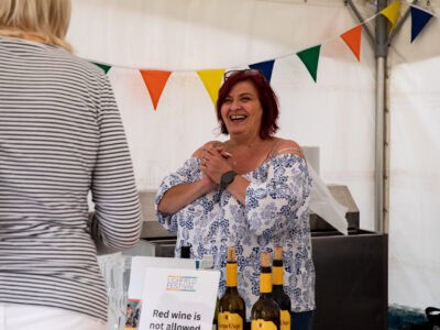 Lichfield Festival Bar A Festival volunteer smiles as she serves a customer at the bar. Bright bunting surrounds the marquee.