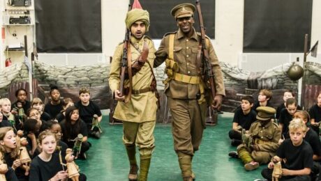 Two actors stand dressed in soldier uniforms, surrounded by school children