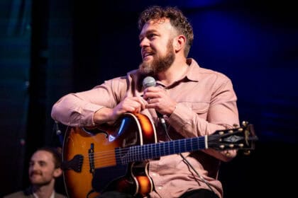 A man sits at a guitar with a microphone