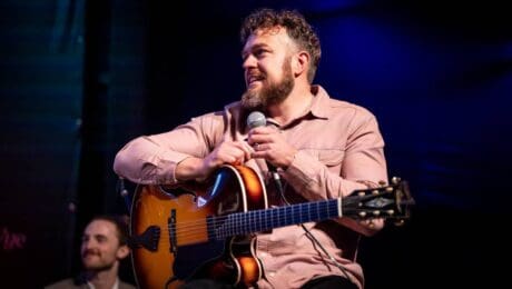 A man sits at a guitar with a microphone