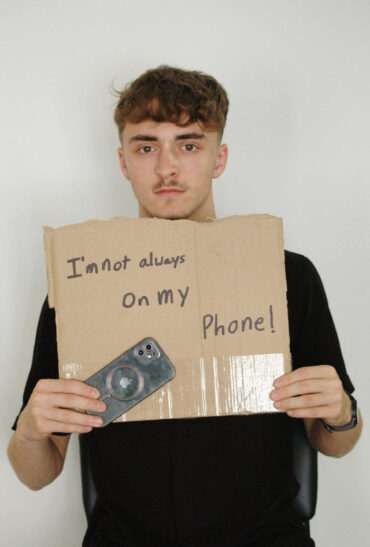 A man stands holding a sign that reads 'i'm not always on my phone'