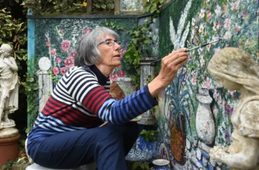 A woman crouches painting on a multicoloured wall